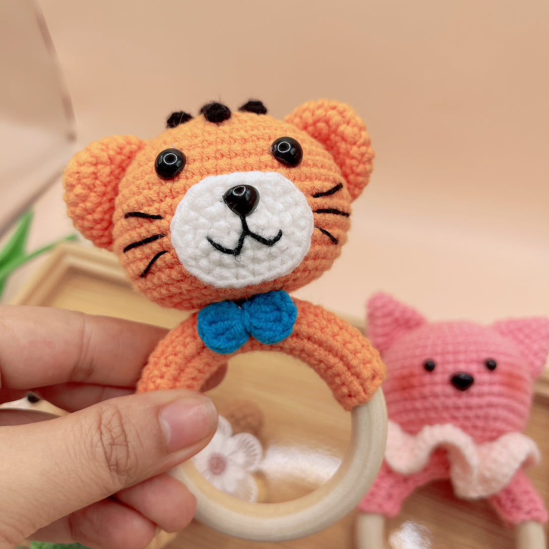 Stitchery Zone animal crochet rattle in orange tiger design with blue bow held by hand