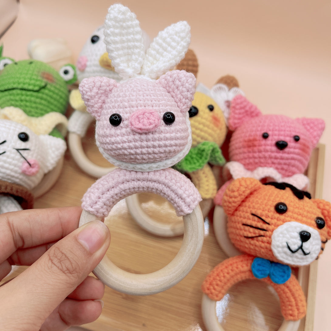 Hand holding a pink animal crochet rattle with bunny ears from Stitchery Zone baby toy collection