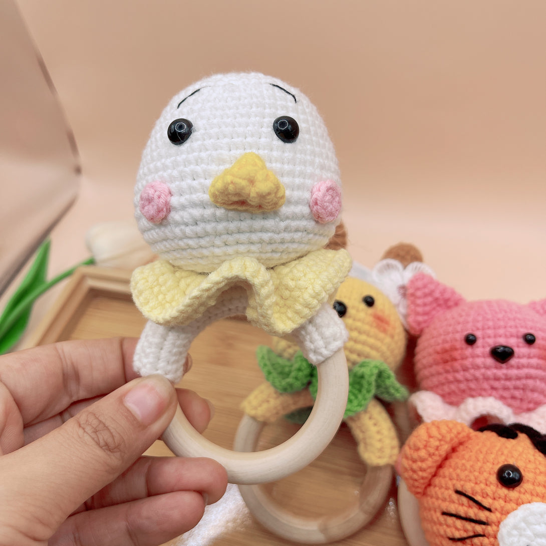 Hand holding a white and yellow Animal Crochet Rattle shaped like a chick with other crochet rattles in the background