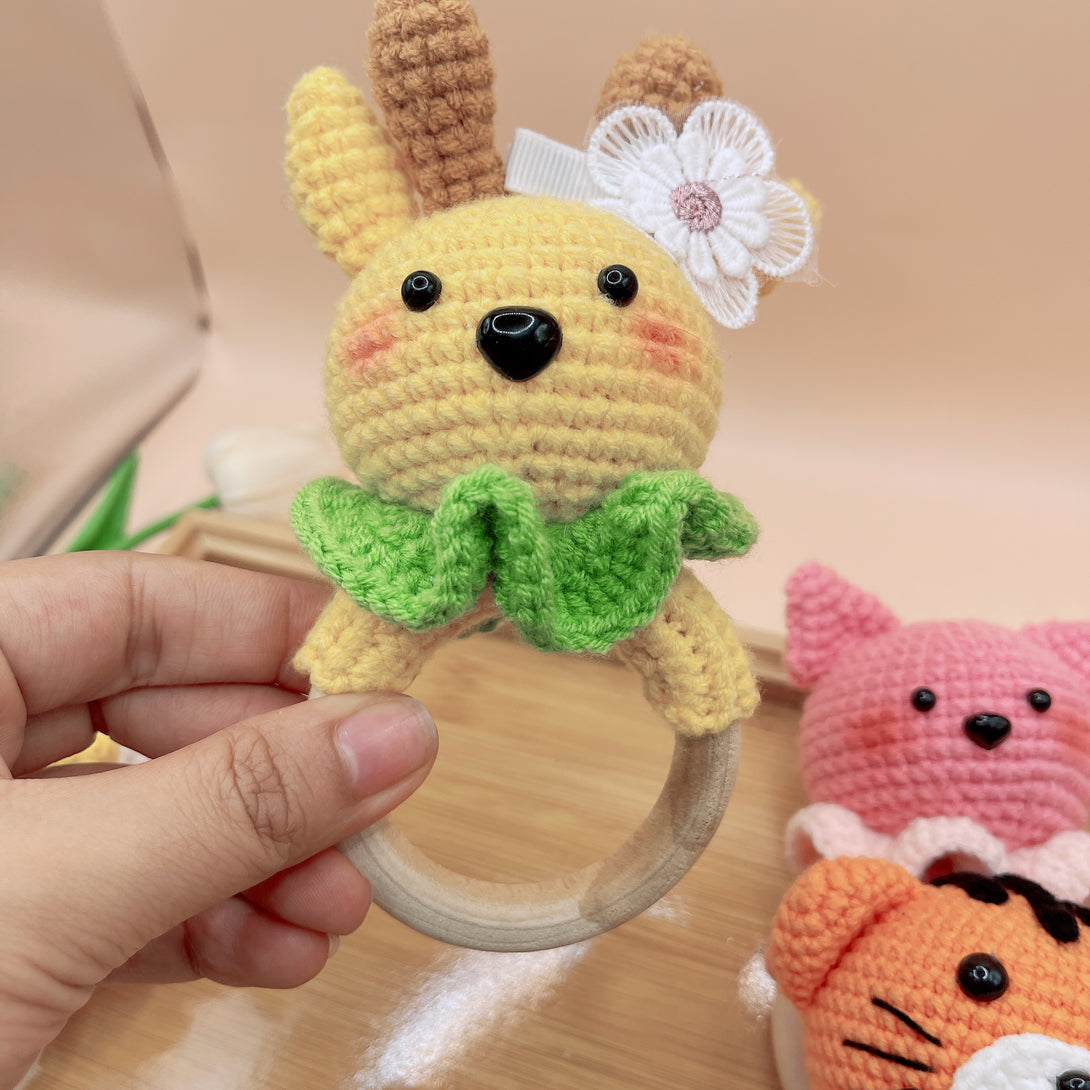 Hand holding yellow Animal Crochet Rattle baby toy with flower and green collar by Stitchery Zone