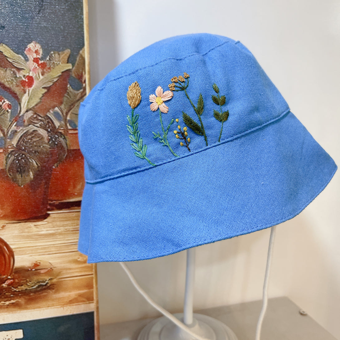 Stitchery Zone Garden Linen Baby Hat in blue with embroidered floral design on front