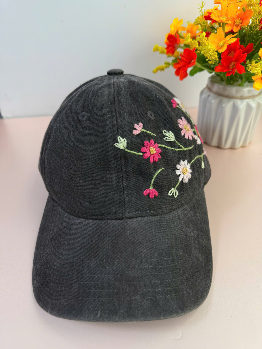 Black cap with colorful daisy hand embroidered hat flowers on front by Stitchery Zone