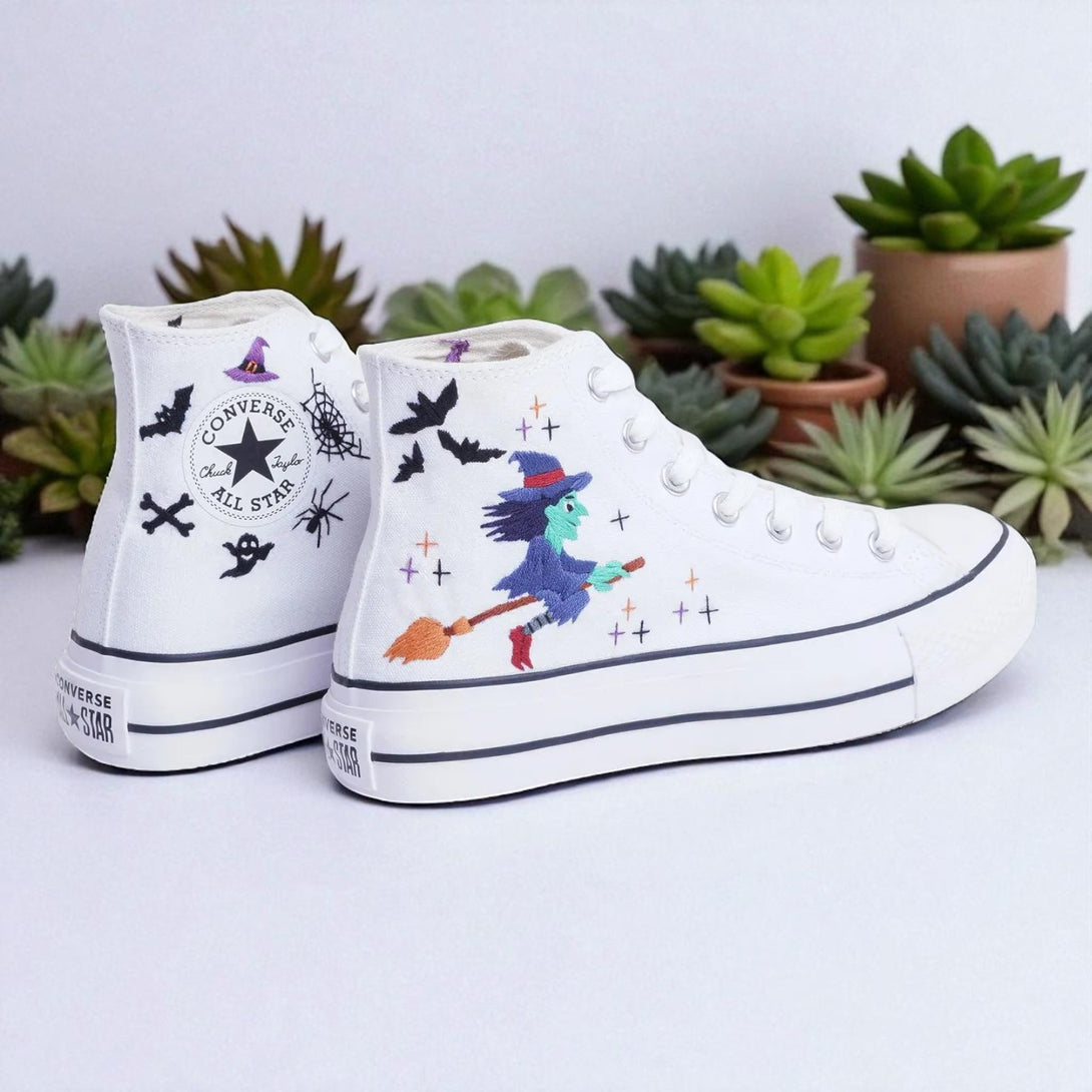 White embroidered Witch Converse high top shoes featuring a green witch on a broom with bats and spider web accents
