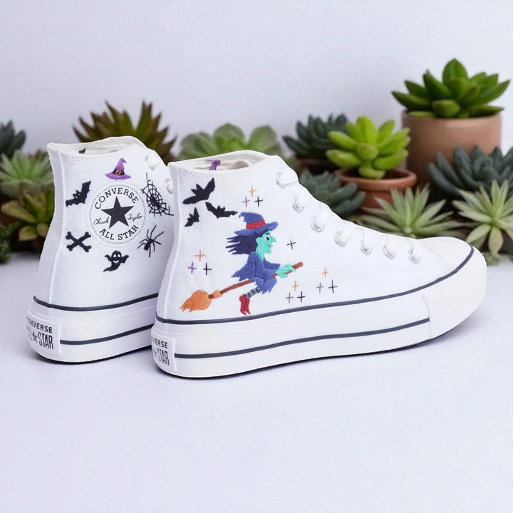 White embroidered Witch Converse high top shoes featuring a green witch on a broom with bats and spider web accents