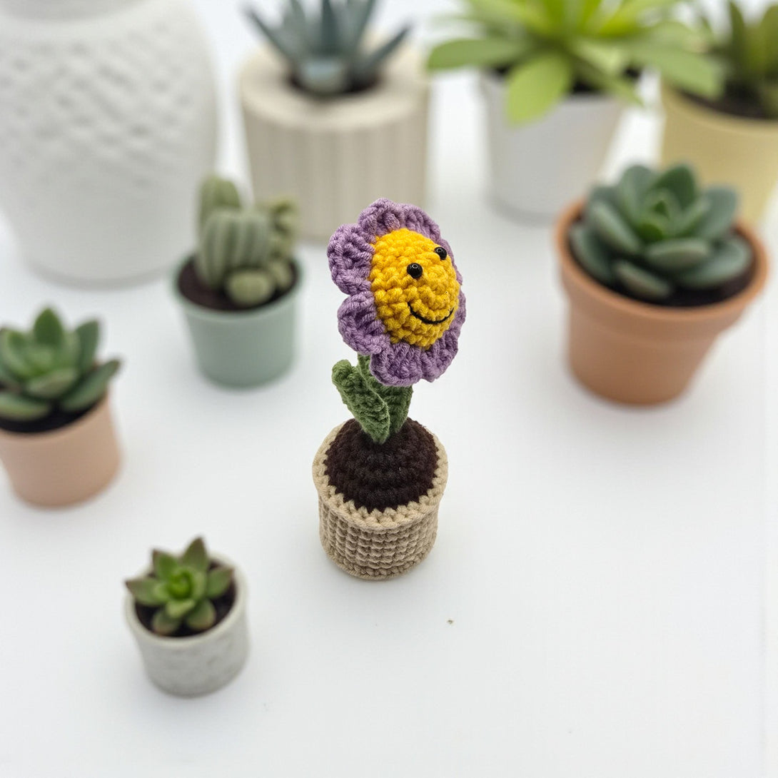 Crochet flower pot featuring a vibrant flower and textured pot, surrounded by small plants