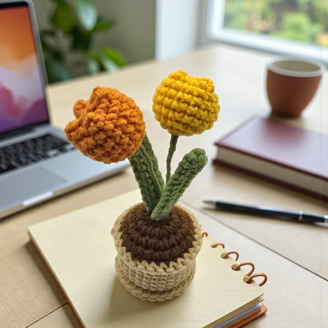 Crochet tulip arrangement in a pot on a desk next to a laptop and notebook