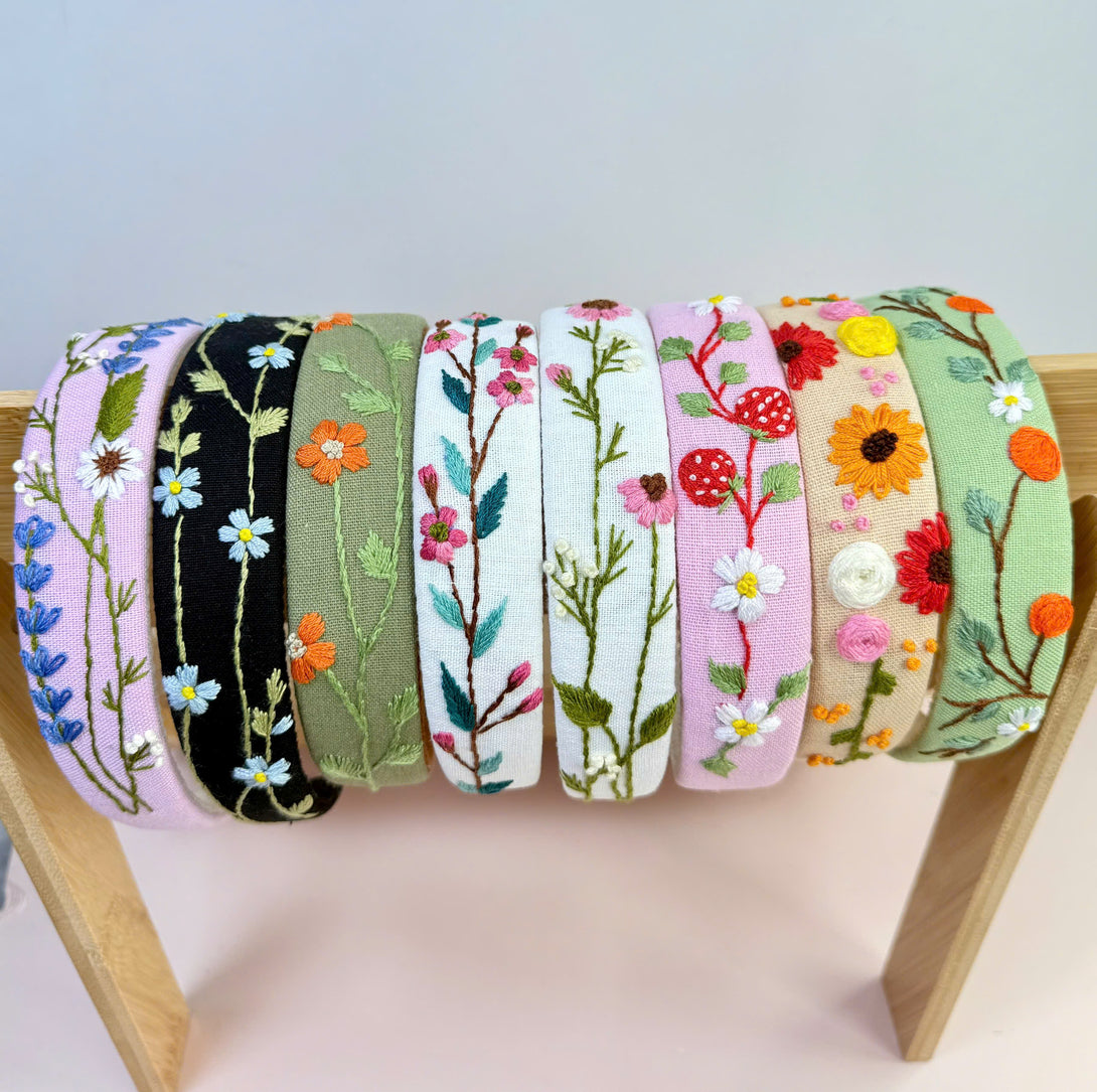 Stitchery Zone embroidered custom headbands with colorful floral designs displayed on wooden stand