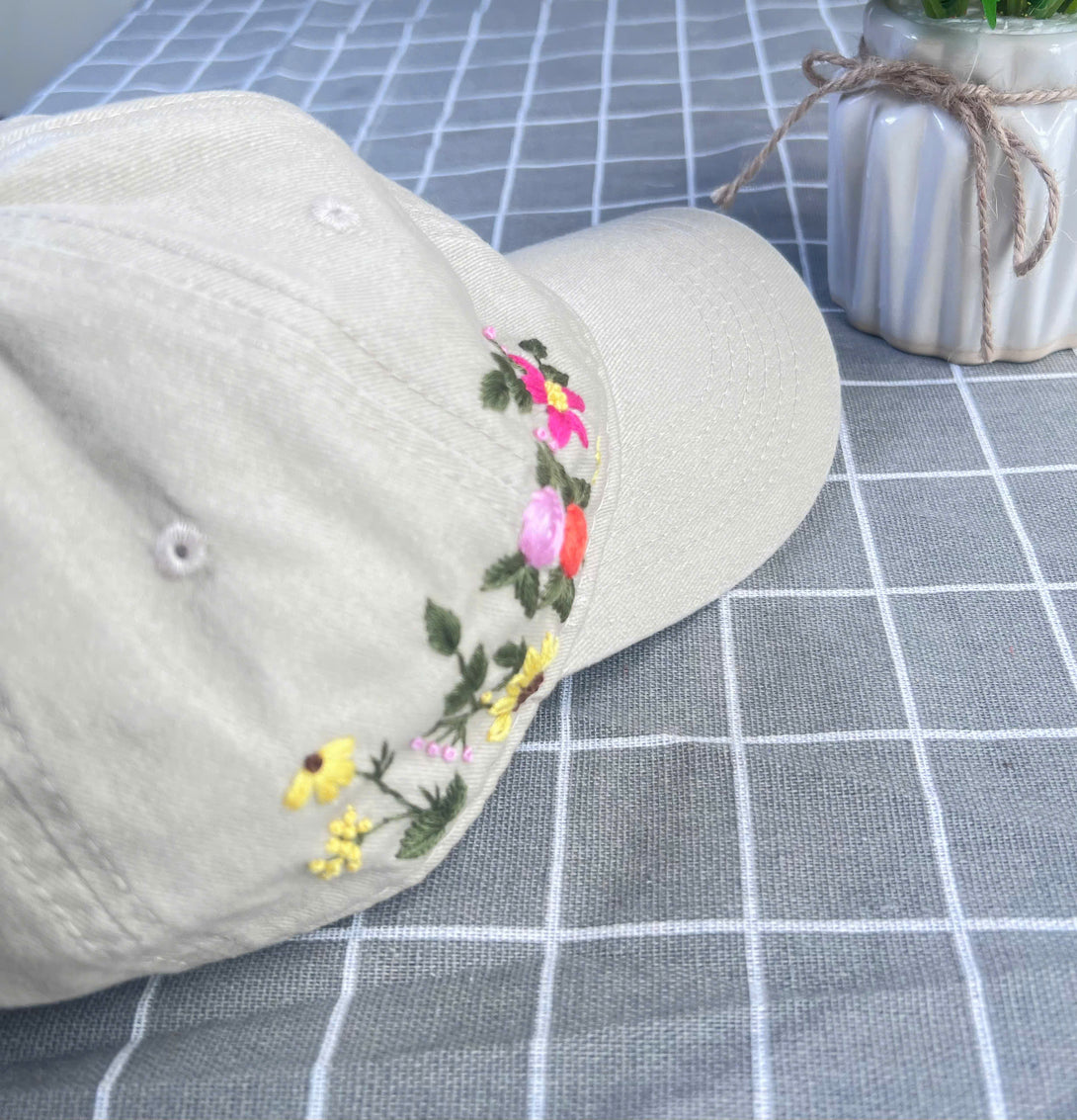 Stitchery Zone beige Embroidered Hat with colorful floral design on checkered tablecloth