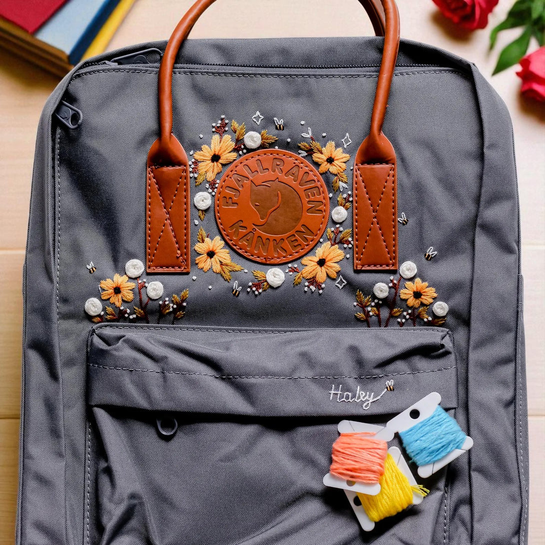 Stitchery Zone Fjallraven Kanken Backpack gray with leather handles embroidered yellow flowers and colorful thread spools