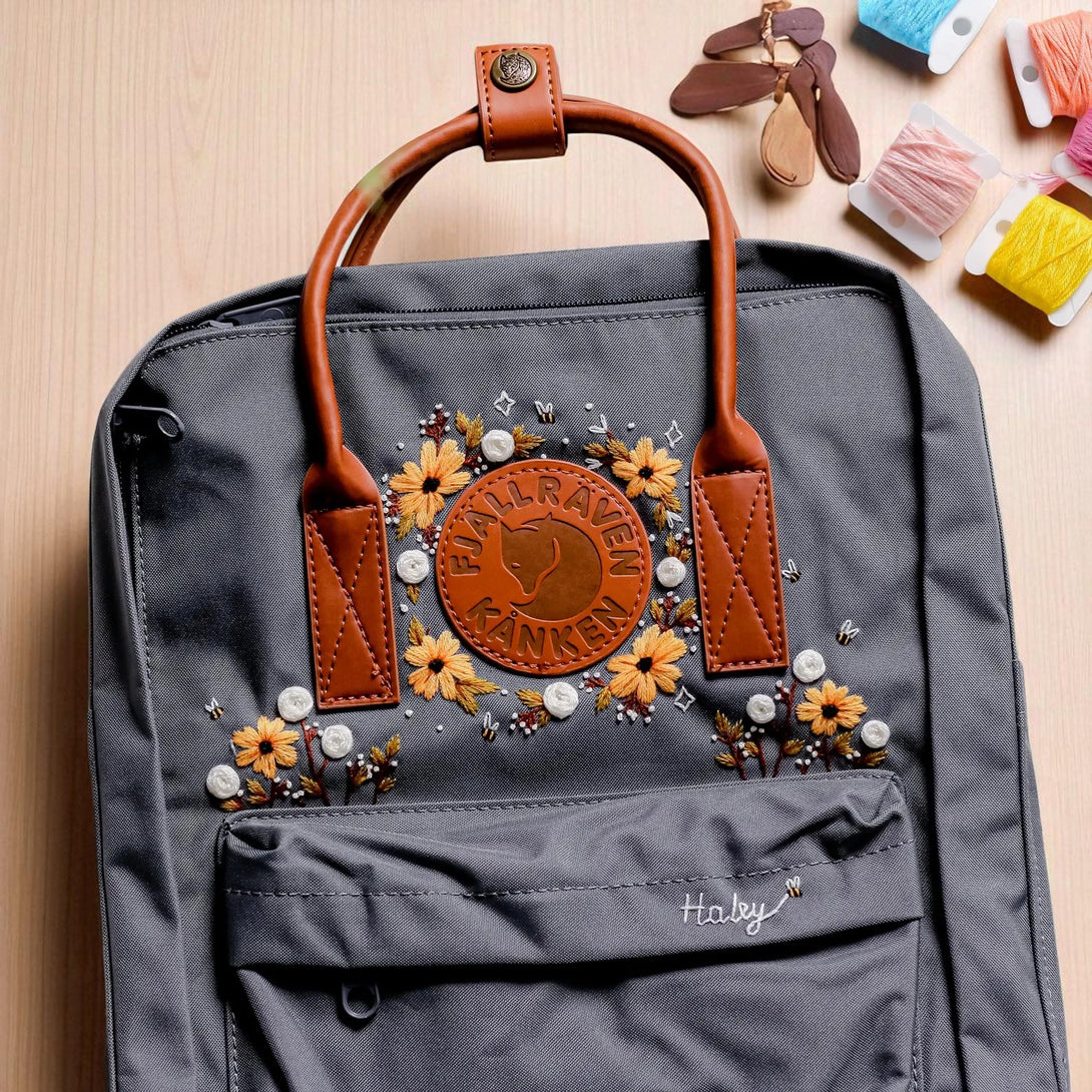 Stitchery Zone Fjallraven Kanken Backpack gray with leather handles embroidered yellow flowers around logo and front pocket