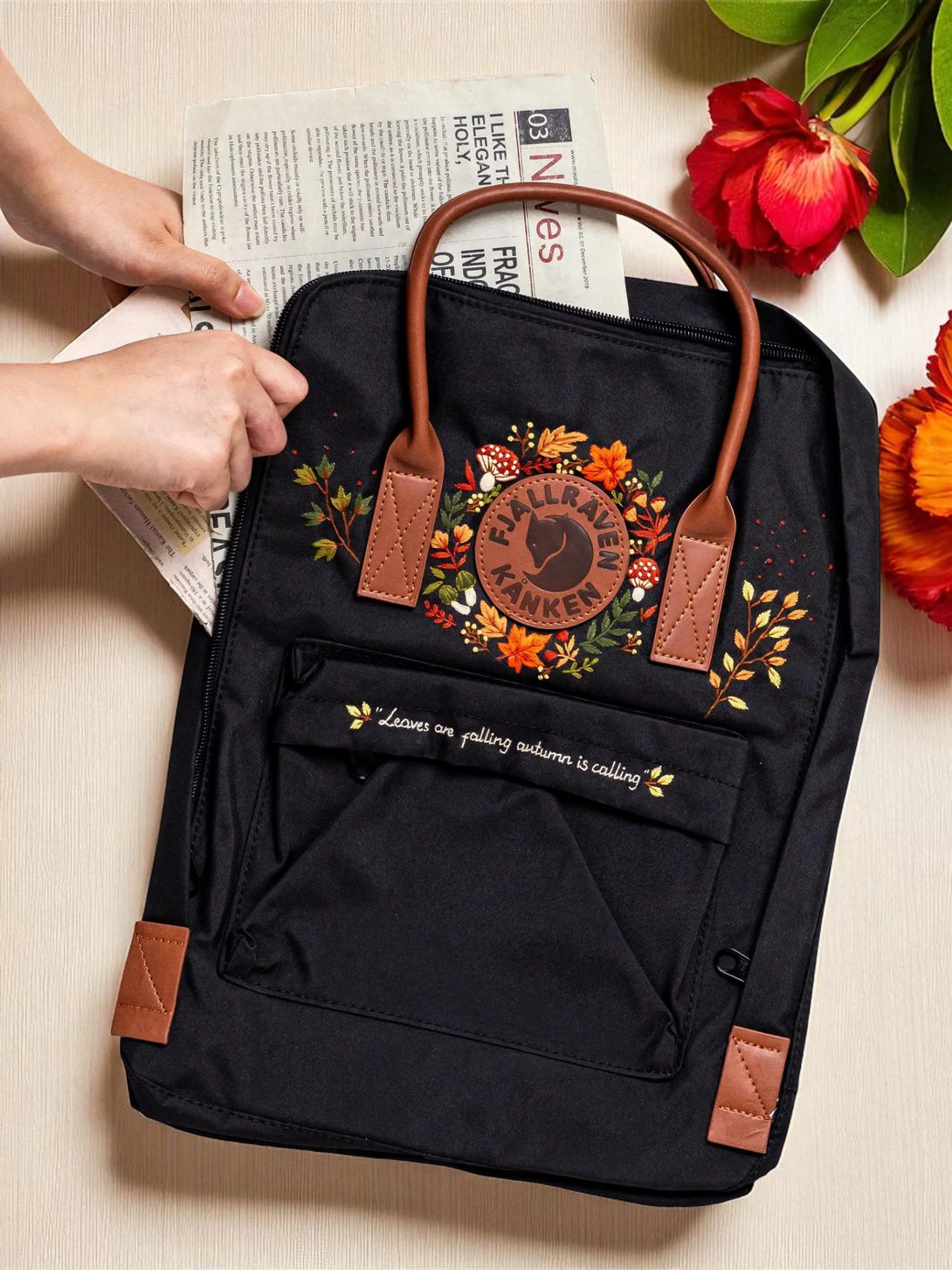 Classic Fjallraven Kanken Backpack black with autumn floral embroidery and brown leather handles on table