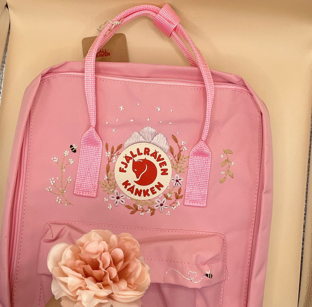 Pink personalized children's backpack by Stitchery Zone with floral embroidery and flower accessory