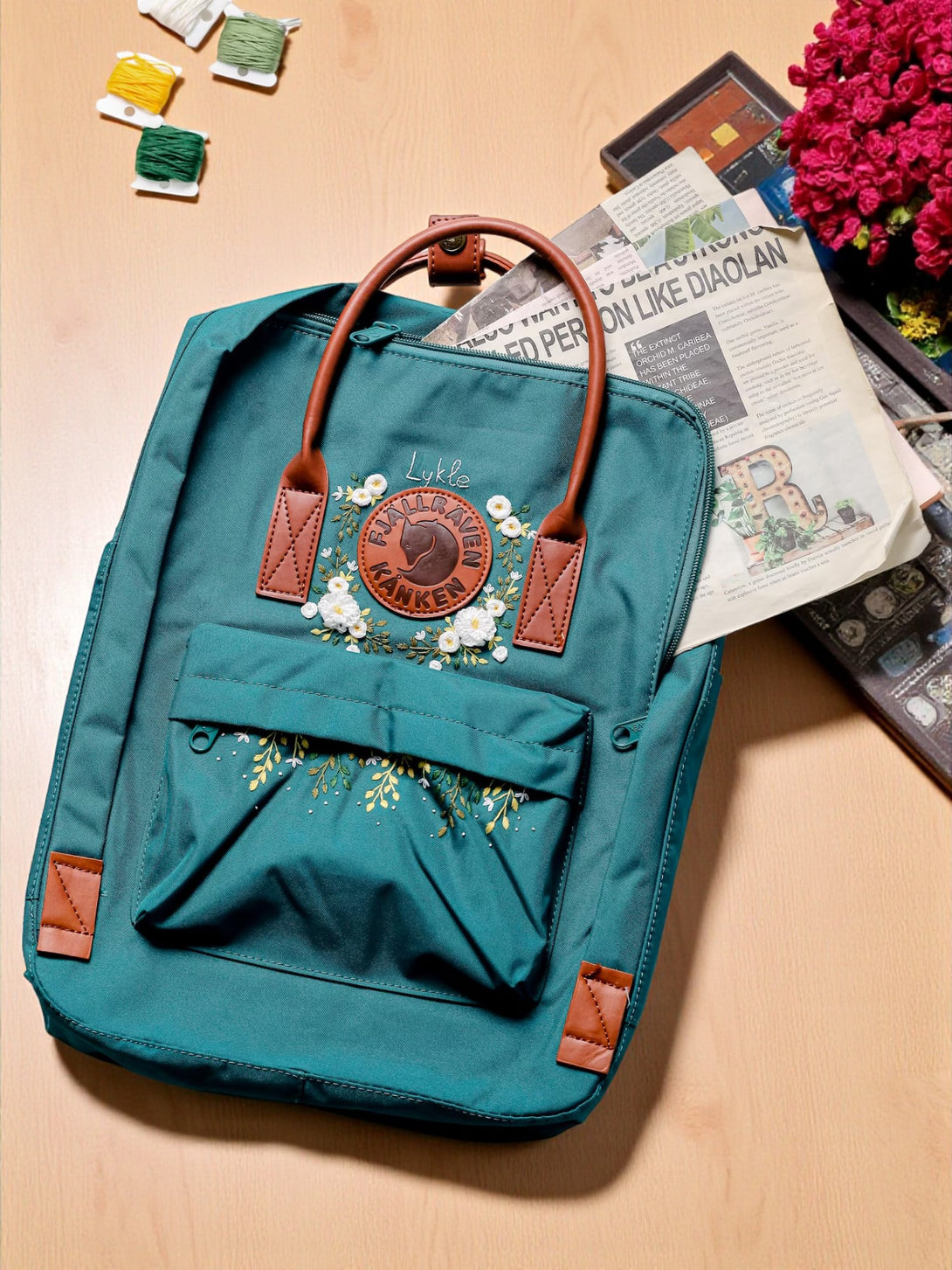 Stitchery Zone teal school backpack with floral embroidery and leather accents on a wooden table