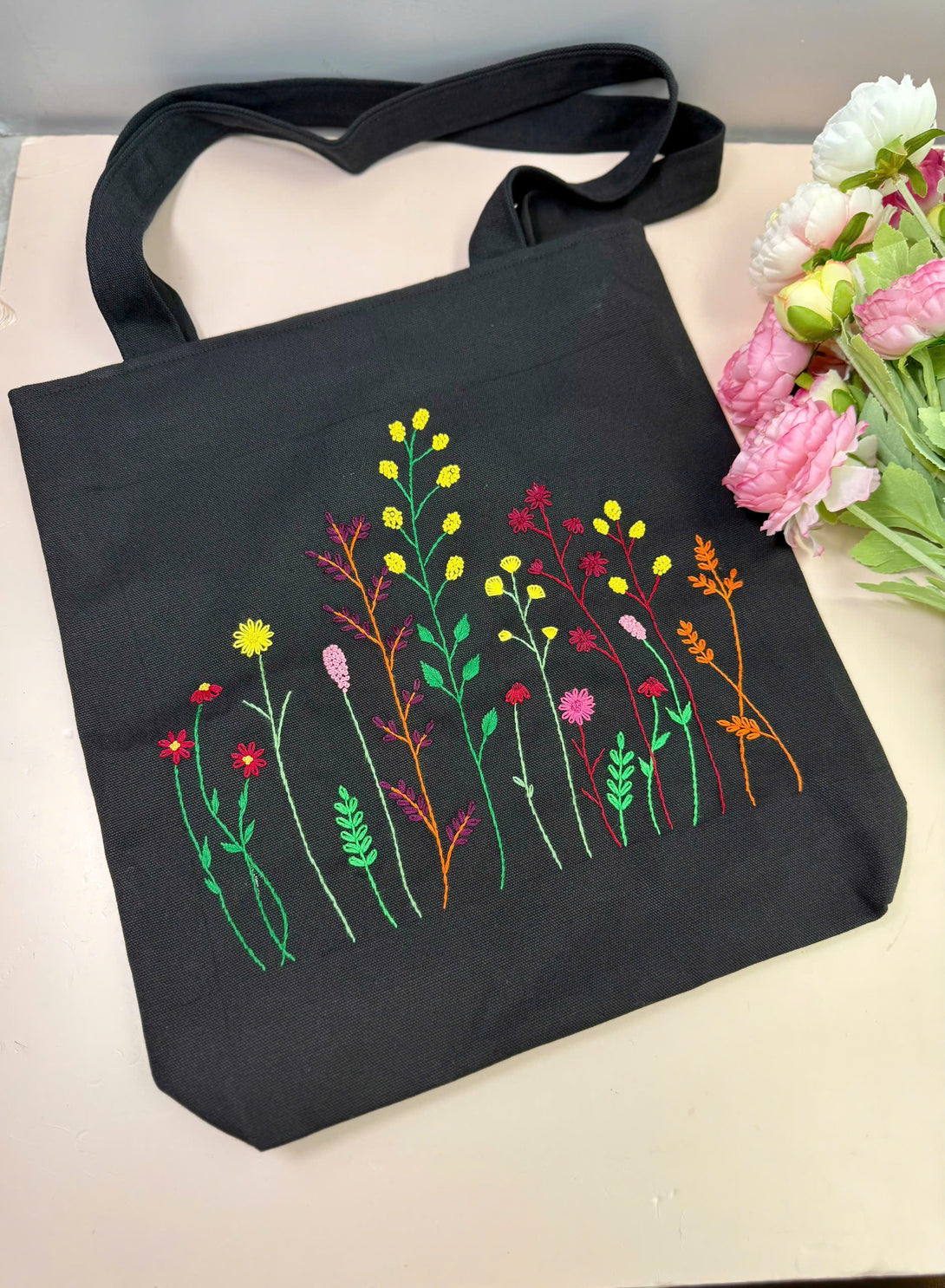 Stitchery Zone black bag with colorful floral embroidery tote design featuring various flowers and green stems