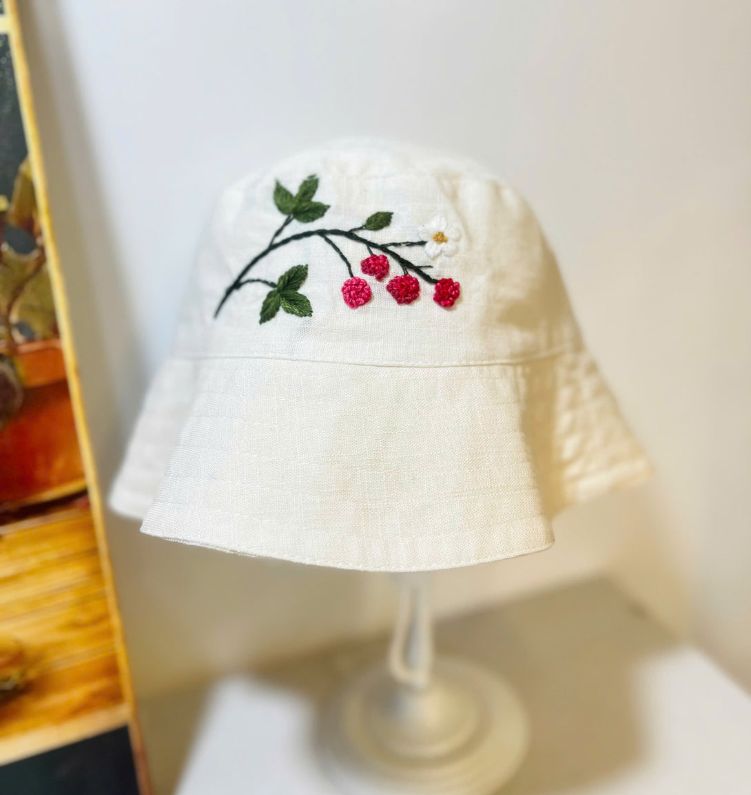 Hand Embroidered Berry Linen Baby Hat by Stitchery Zone featuring red berry and green leaf embroidery on white linen
