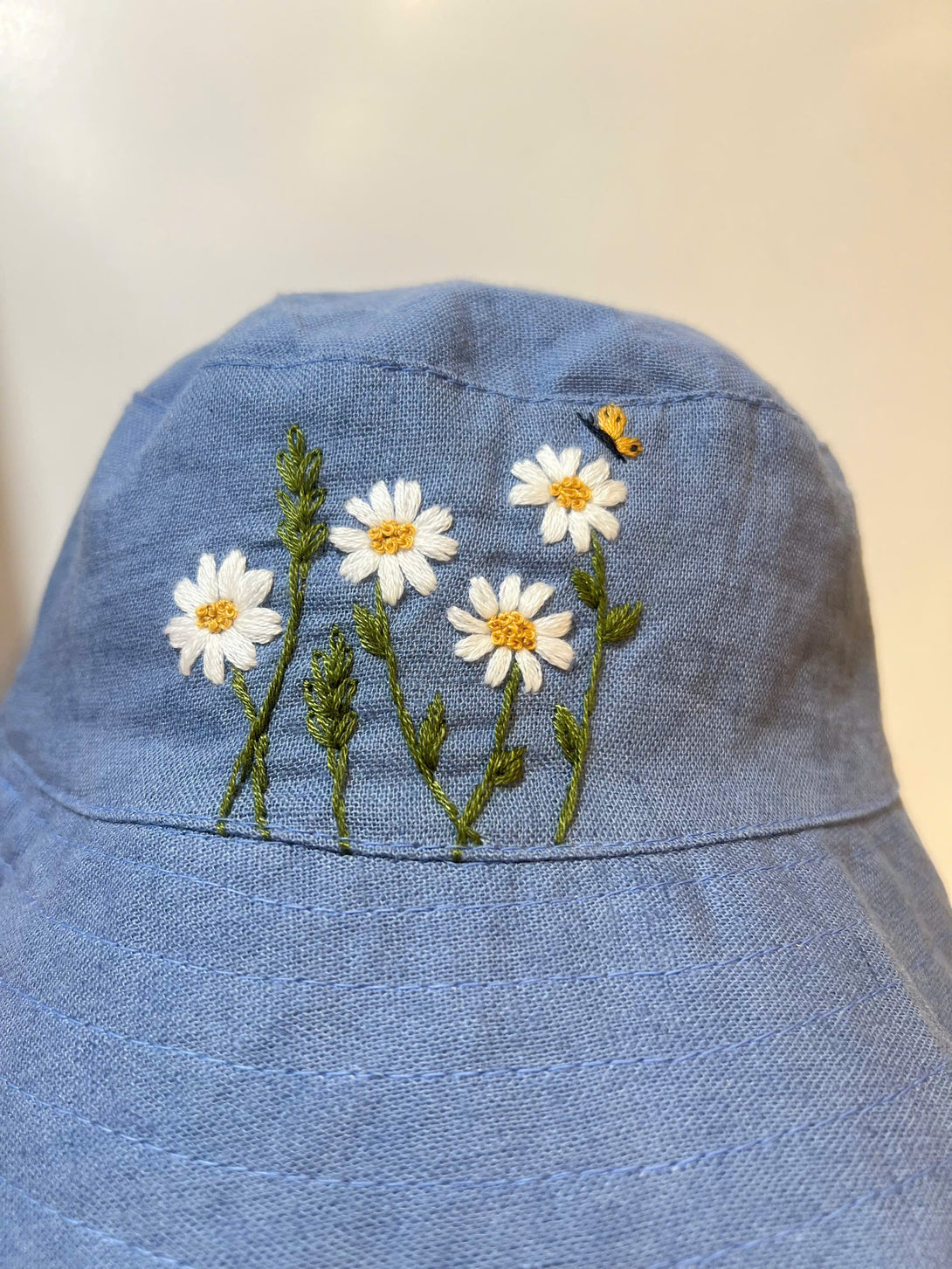 Hand Embroidered Daisy and Bee Linen Baby Hat in blue with white daisy flowers and a small embroidered bee
