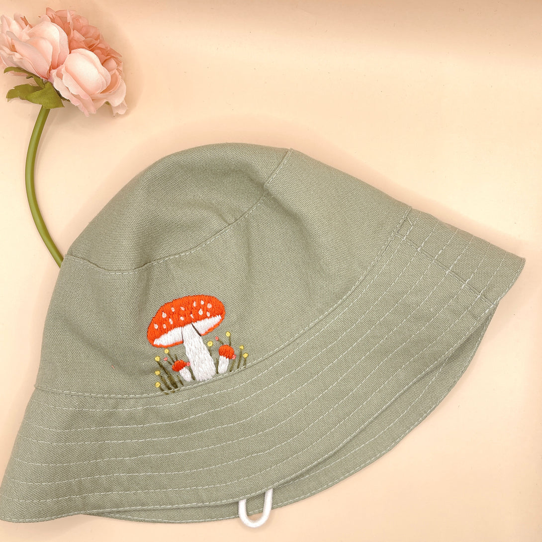 Hand Embroidered Mushroom Linen Baby Hat by Stitchery Zone in sage green with orange mushroom design
