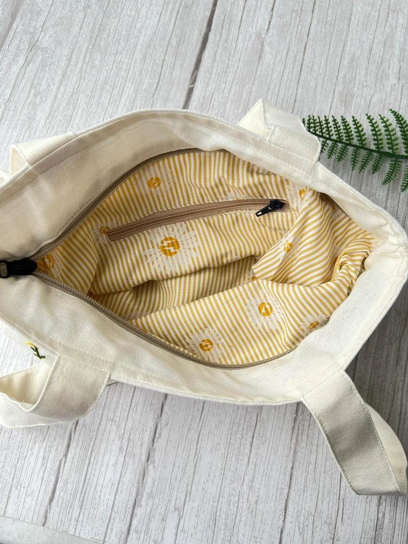 Interior view of Lavender Garden Hand Embroidered Tote Bag by Stitchery Zone with striped yellow lining and zippered pocket