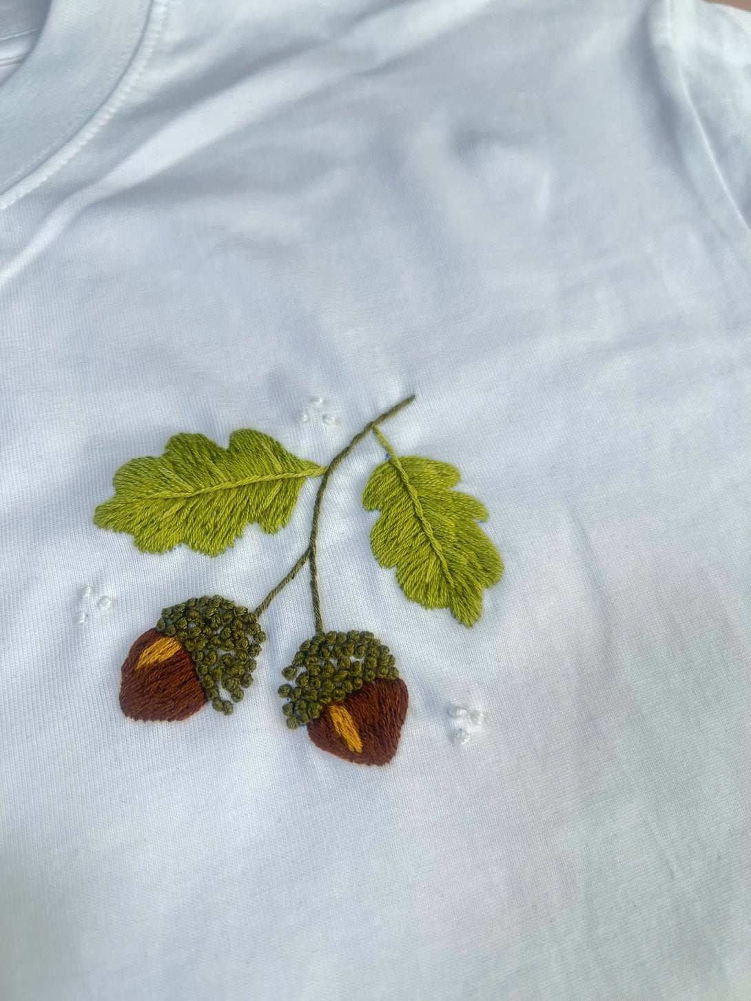 White t-shirt from Stitchery Zone with detailed nature inspired embroidered shirt design of green leaves and acorns