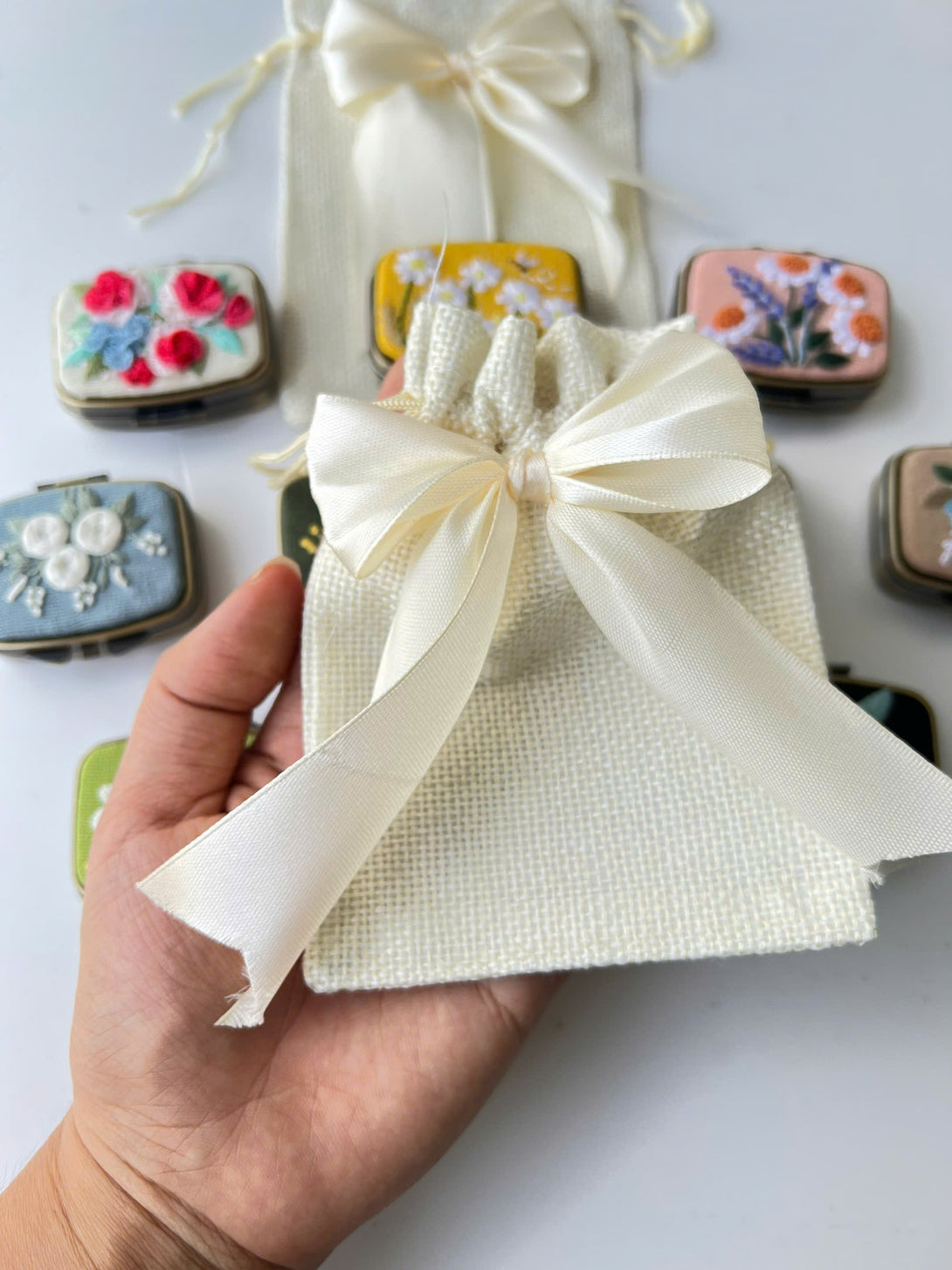 Personalized Embroidered Jewelry Box pouch with white satin bow held in hand with floral embroidered boxes in background