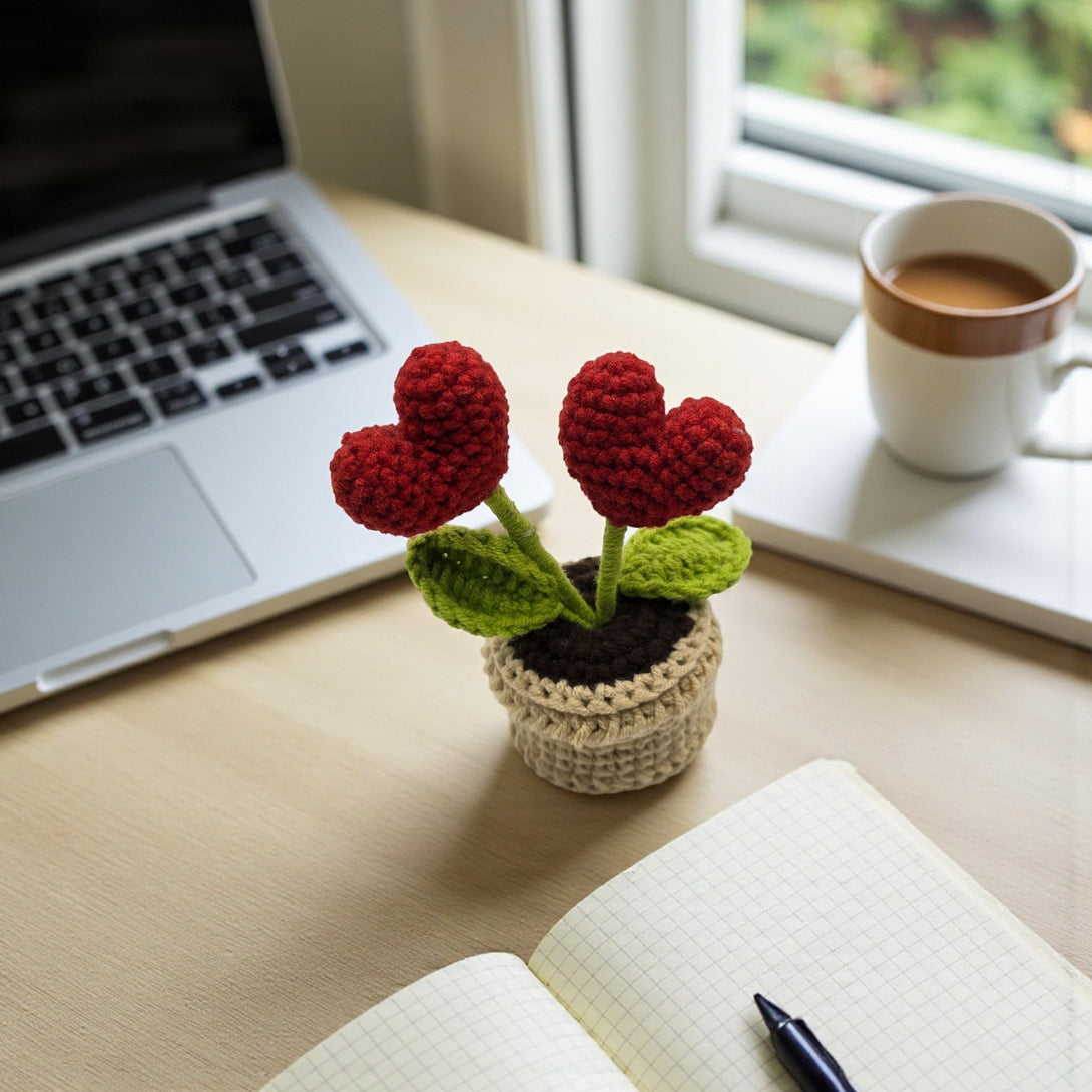 Red heart crochet pot with two red hearts and green leaves on a workspace table