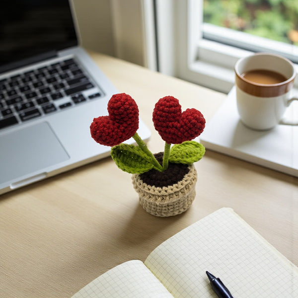 Red heart crochet pot with two red hearts and green leaves on a workspace table