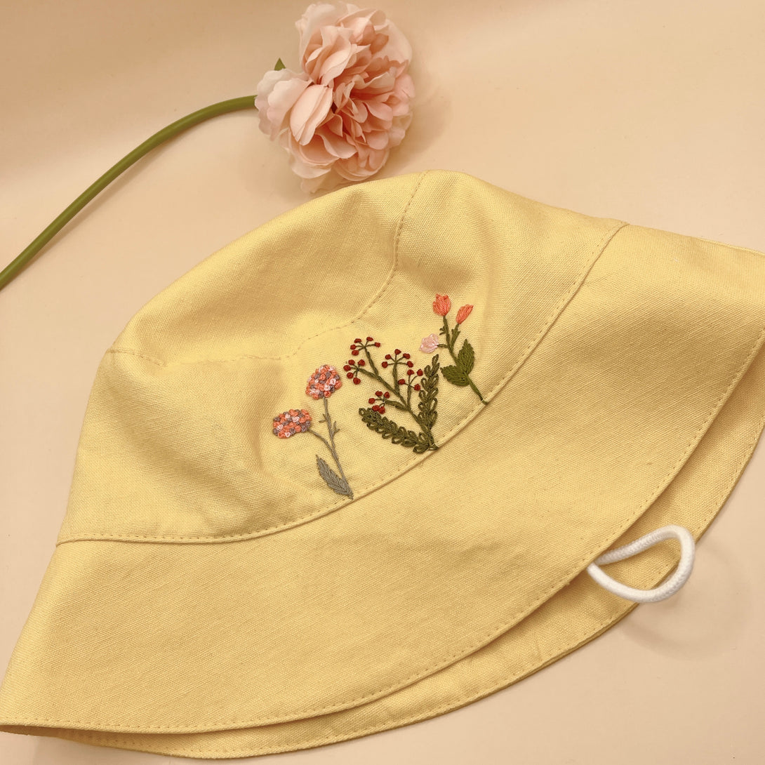 Yellow Embroidered Linen Baby Hat with floral designs by Stitchery Zone on beige background