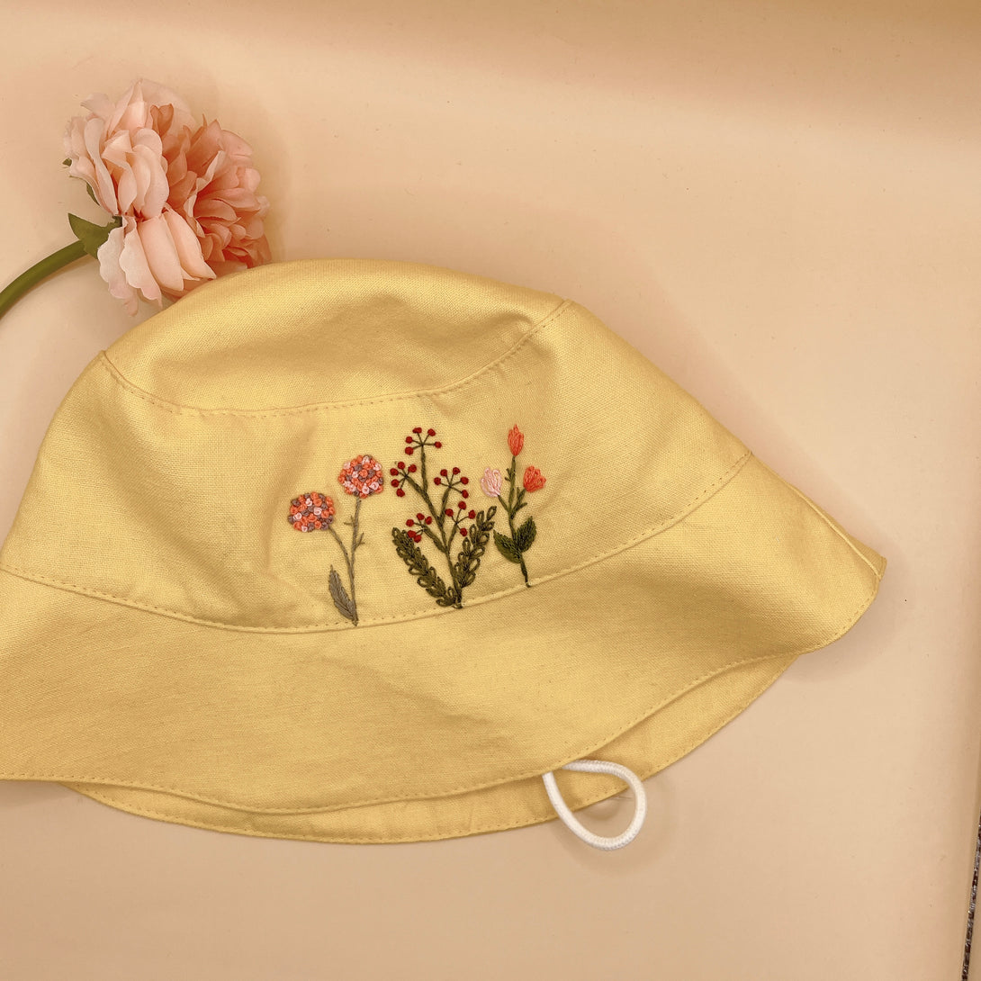 Yellow Embroidered Linen Baby Hat with floral stitch details from Stitchery Zone on beige background