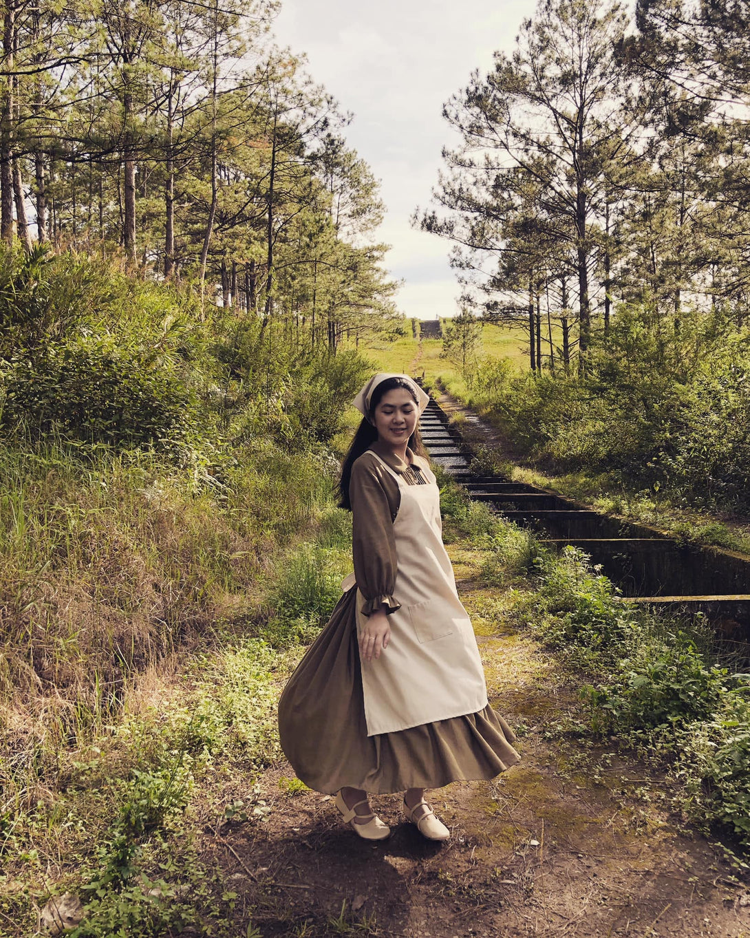 Woman wearing a Vegetable Embroidery Linen Apron by Stitchery Zone standing on a forest path