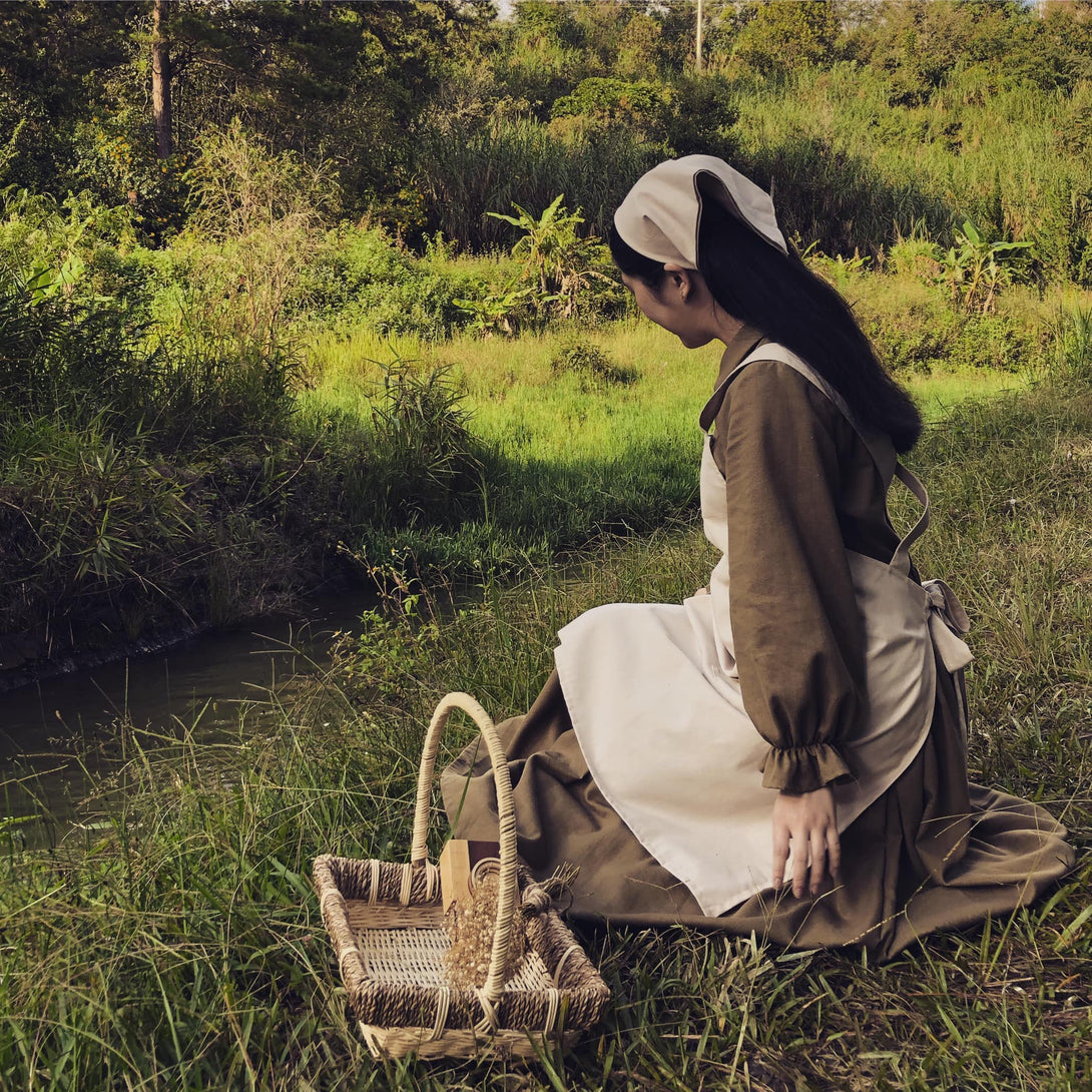 Stitchery Zone Vegetable Embroidery Linen Apron worn by woman sitting outdoors near a basket
